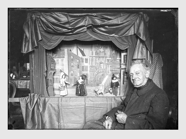 Valeska Kollmann: Joseph Leonhard Schmid hinter seiner Marionettenbühne mit Harlekin und Kasperl Larifari. München, 1900.